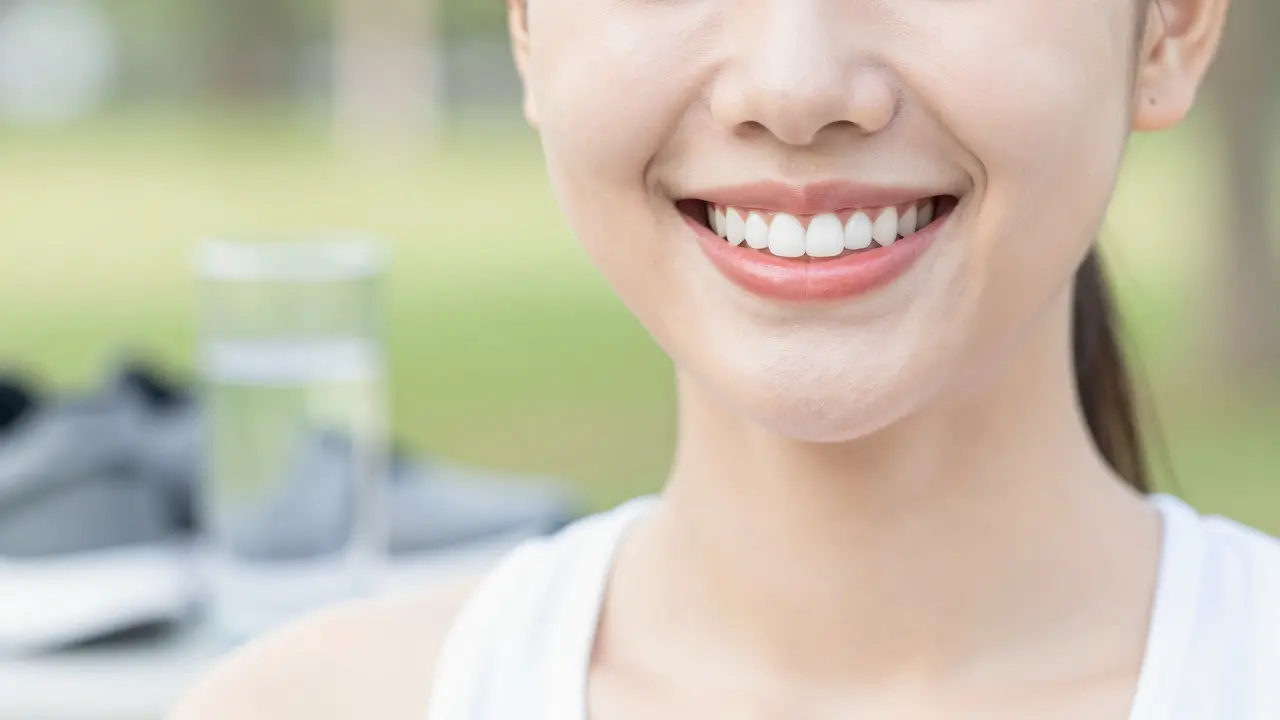 Detail zdravého, bílého úsměvu a zářící pleti člověka v přirozeném denním světle.